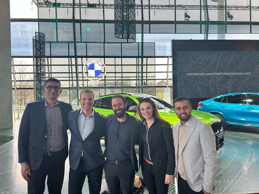 Visit to BMW. A group of business professionals smiling and posing in front of BMW cars inside a modern showroom, showcasing luxury vehicles and innovative automotive design.