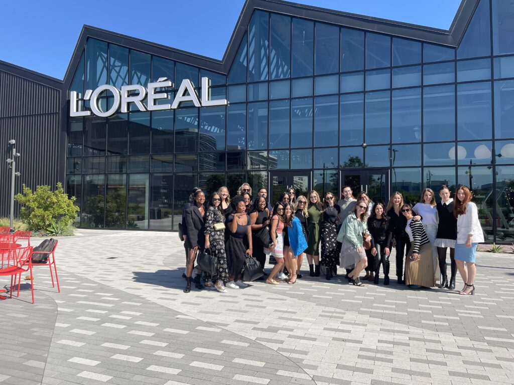 Group of business professionals from FIT visiting the L'Oréal headquarters, sitting at a long conference table, engaged in a presentation with a speaker in a modern and brightly lit meeting room.