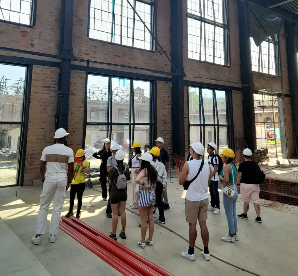 A group of people wearing hard hats on a construction site tour inside an industrial building, discussing architectural design, renovation, and urban development projects.