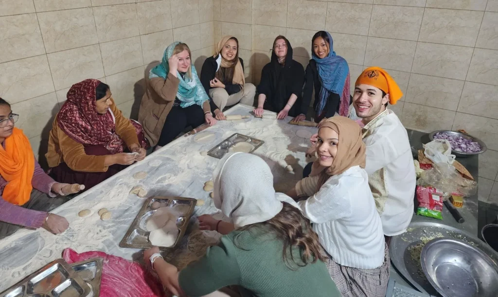 Social impact Montclair U MBA. A diverse group of people, including locals and tourists, sitting together in a kitchen, making traditional bread by hand as part of a cultural cooking experience.