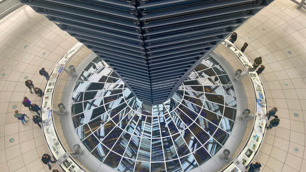 Inside the Reichstag building. Aerial view of the interior of the Reichstag dome in Berlin, Germany, showing the central mirrored cone and surrounding walkway where visitors observe informational displays, reflecting the modern architecture and transparency of the German parliament building.