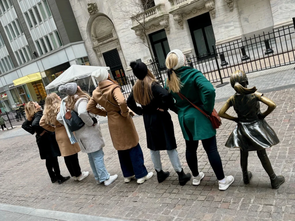 Group of women posing confidently beside the Fearless Girl statue on Wall Street in New York City, celebrating empowerment, gender equality, and women in leadership.