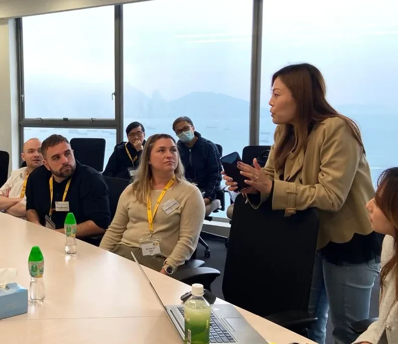 Strong, independent Businesswoman leading a discussion during a corporate meeting in a conference room with diverse international participants, overlooking a cityscape view through large windows.