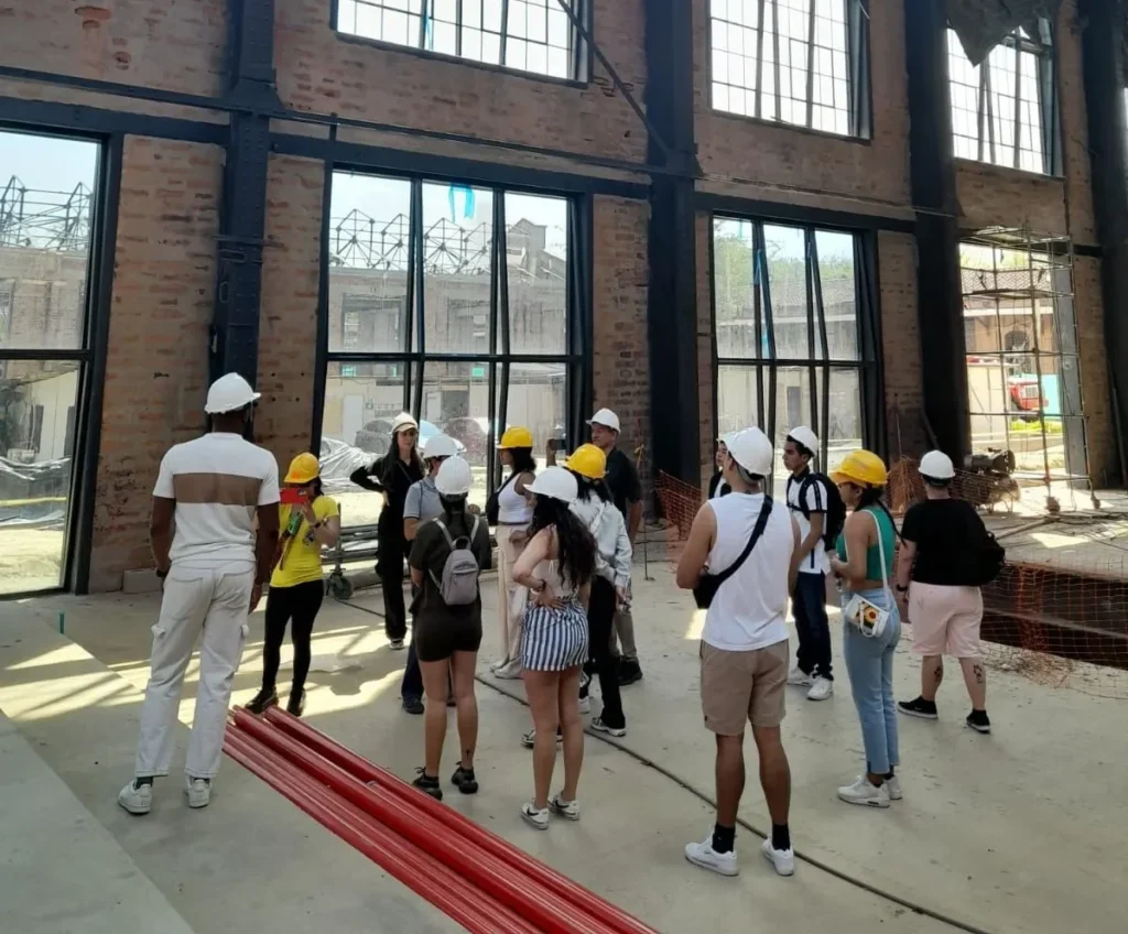 Mercy University in Medellin. Group of people wearing hard hats on a construction site tour inside an industrial building, discussing architectural design, renovation, and urban development projects.