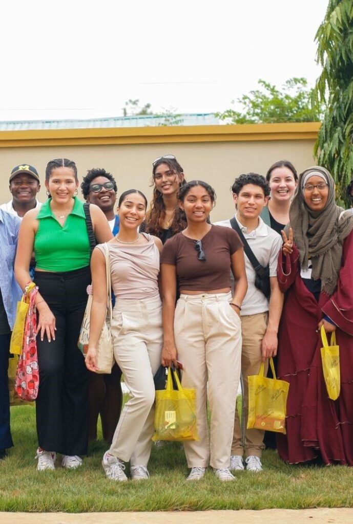 Cornell students smiling during a group trip in Ghana, holding yellow gift bags.