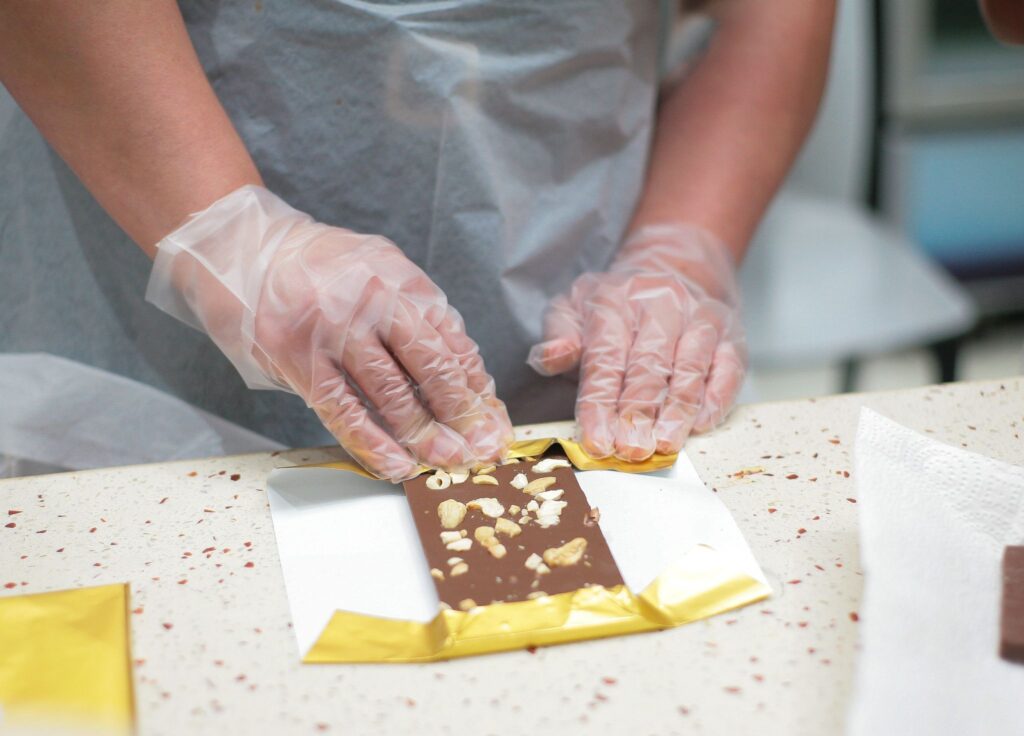 Hands in gloves wrapping a chocolate bar topped with nuts in Ghana.