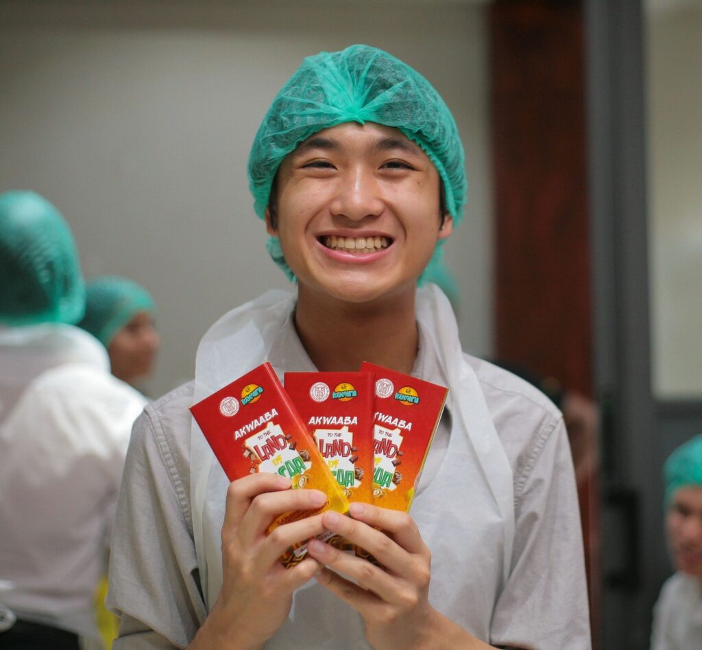 Smiling person holding bars of chocolate with Ghana-themed packaging.