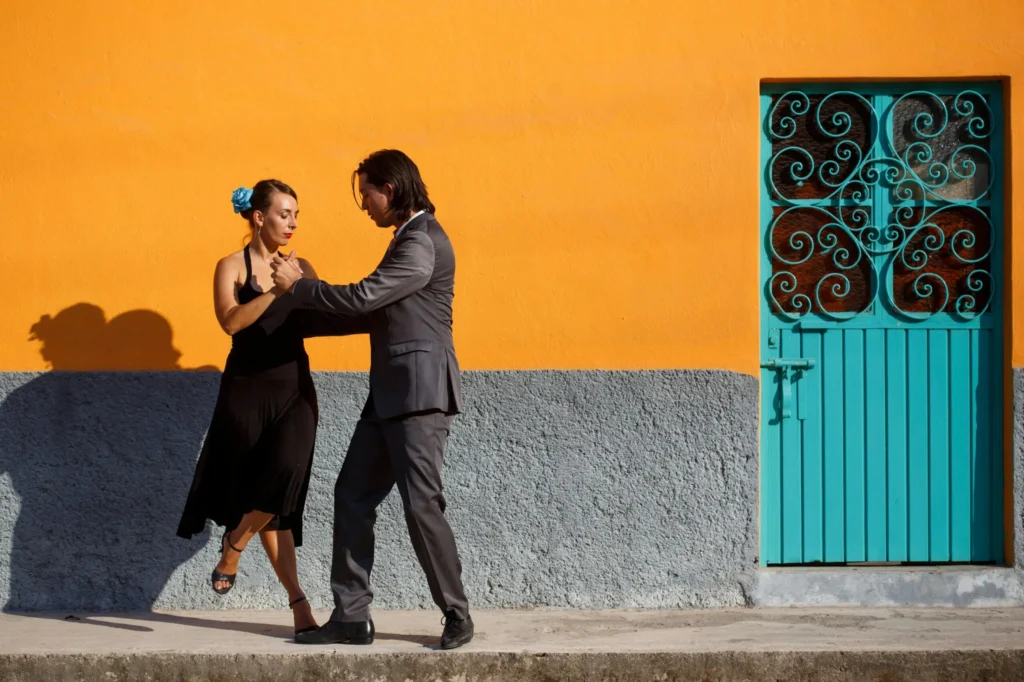 Couple dancing the tango in front of a colorful orange wall.