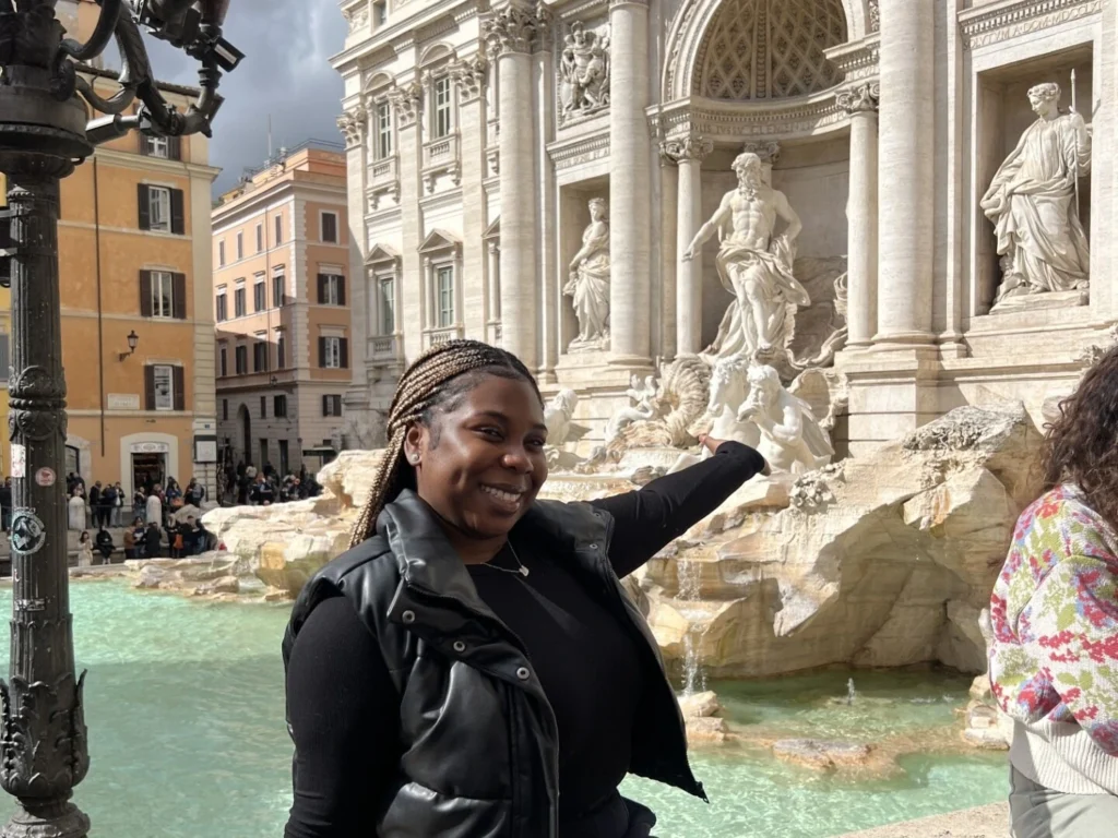 Woman smiling and pointing at the Trevi Fountain in Rome.