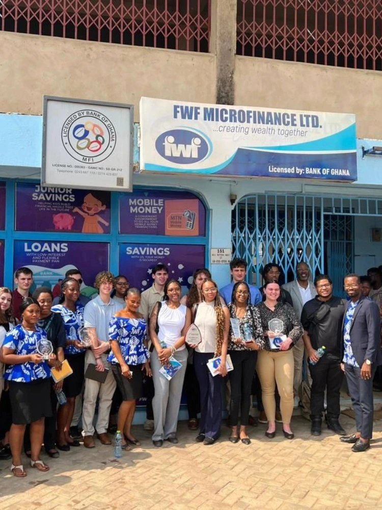 Group photo of international students and professionals in front of FWF Microfinance Ltd. in Ghana, learning about microfinance, mobile money, and banking services.