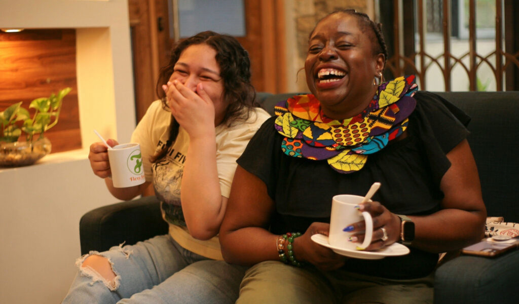 Two women laughing and enjoying coffee together in a cozy living room.