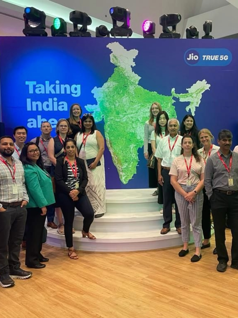 A group of people stands on a platform in front of a map of India. A sign reads "Taking India ahead" with the Jio logo and "True 5G."