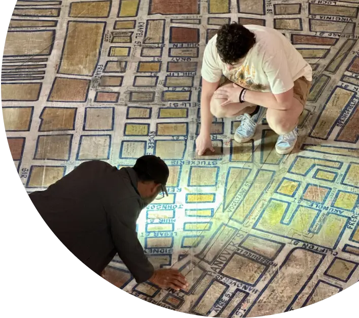 Two People Examining a Large Historical Map on the Floor